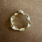 A gold ring with a twisted, organic shape, and a gray diamond photographed on a brown textured surface.