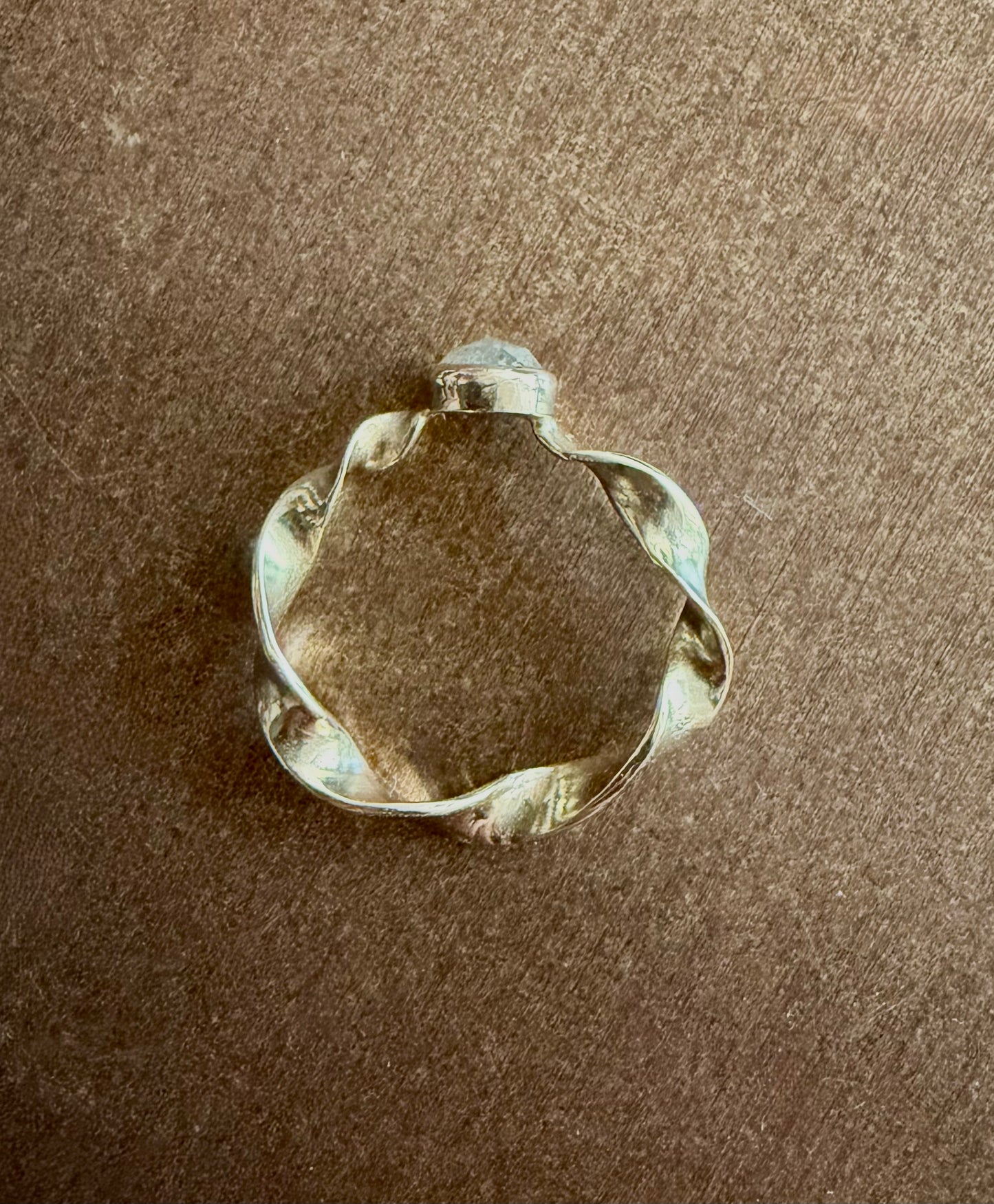 A gold ring with a twisted, organic shape, and a gray diamond photographed on a brown textured surface.