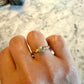 A gold ring with a rosecut gray diamond worn on a person's finger, shown against a marble  background.
